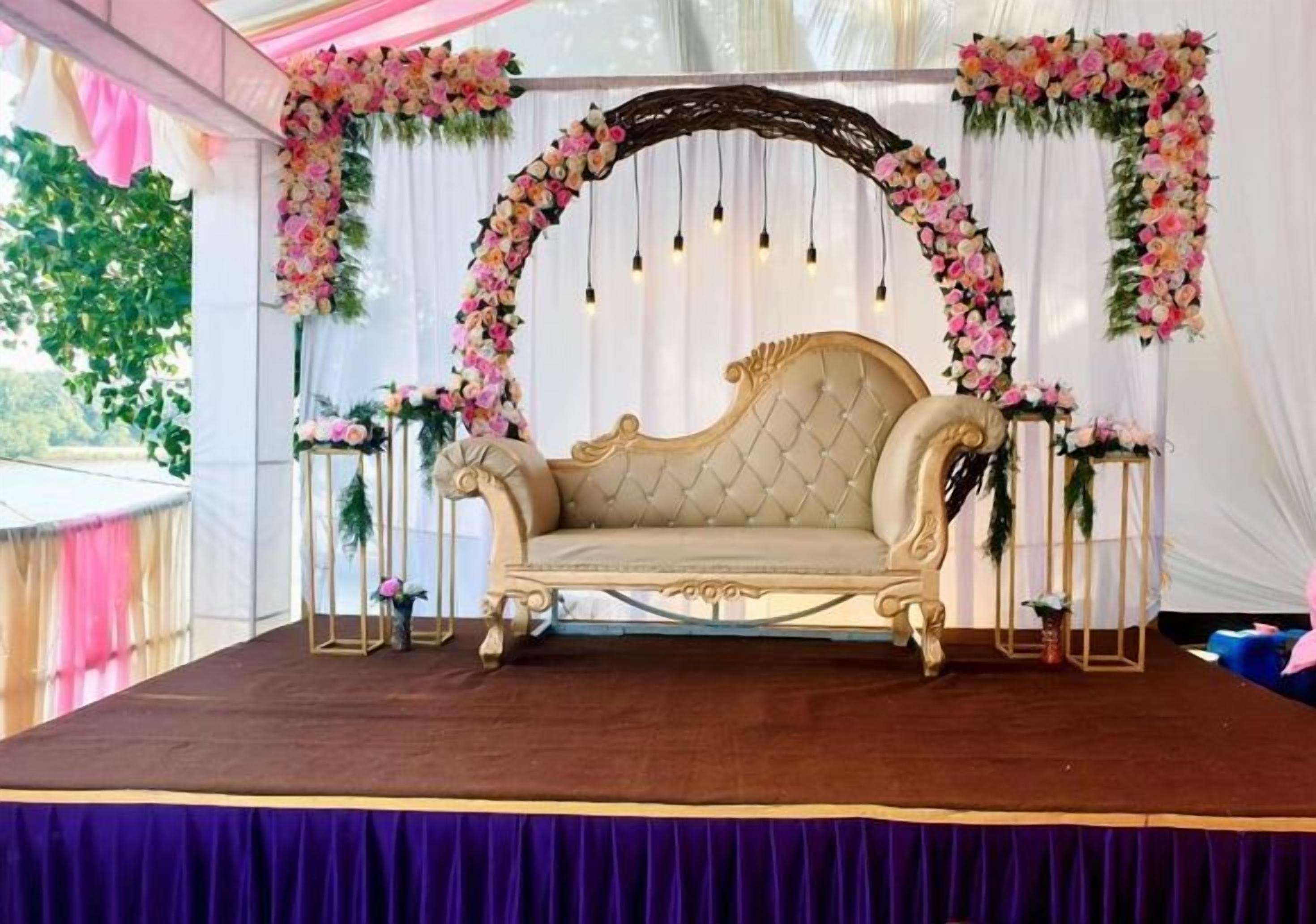 A stage with a tufted sofa, floral arches, and draped curtains.