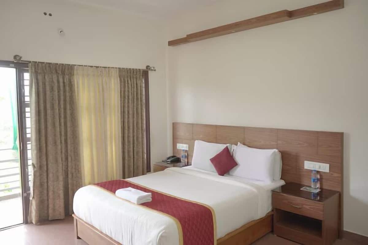 A hotel room with a large bed, wooden headboard, bedside tables, and a window with curtains.