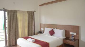Una habitación de hotel con una cama grande, cabecero de madera, mesitas de noche y una ventana con cortinas.
