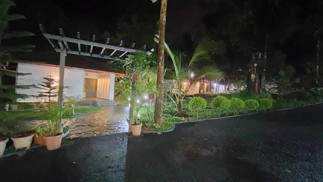 A nighttime view of a building with a covered entrance, potted plants, and a paved pathway leading to the entrance.