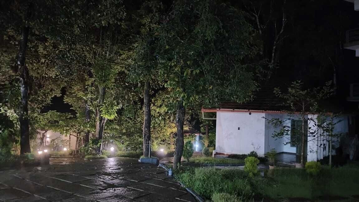 A nighttime scene with a paved driveway, a small white building with a red roof, and trees surrounding the area.