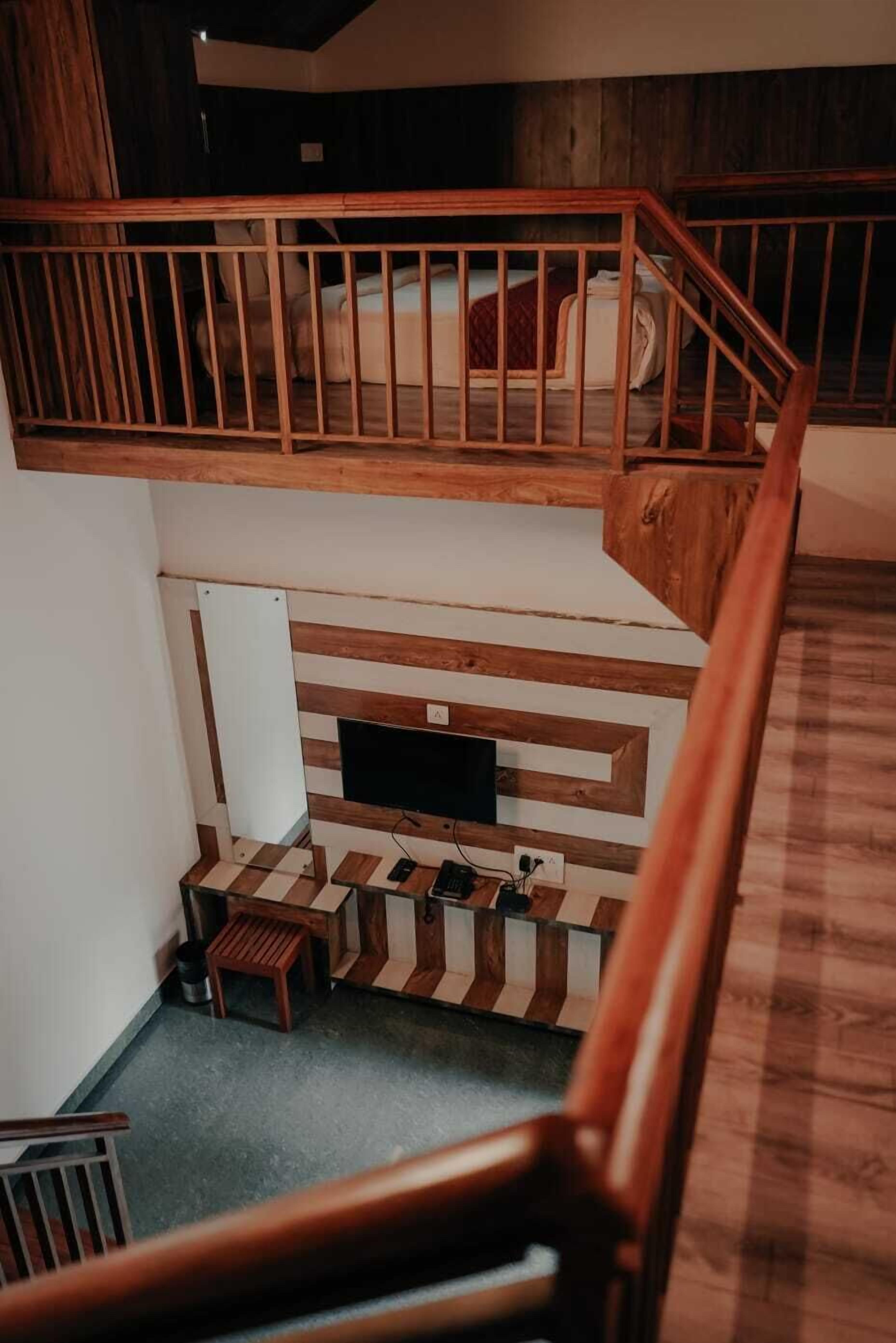 Ett sovrum i loftstil med en trätrappa, en säng, en tv och en liten sittgrupp.