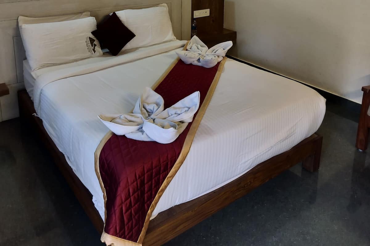 A neatly made bed with white linens and a red quilted bedspread, a wooden headboard, and a wooden ceiling with exposed beams.