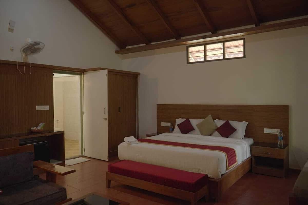 A bedroom with a wooden headboard, a bed with red and white bedding, a bench at the foot of the bed, a bedside table, a wardrobe, and a ceiling fan.