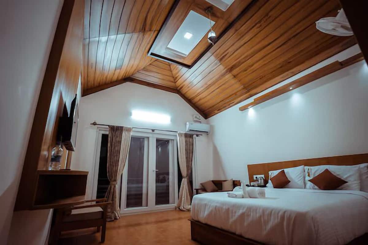 A bedroom with a wooden ceiling, a bed with white bedding, a desk with a chair, and a sliding glass door leading to an outdoor area.