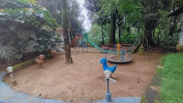 Un parque infantil con tobogán, columpios y una estructura para escalar, rodeado de árboles.