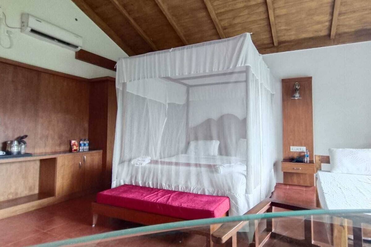 A bedroom with a canopy bed, a wooden wardrobe, a bedside table, and a small desk.
