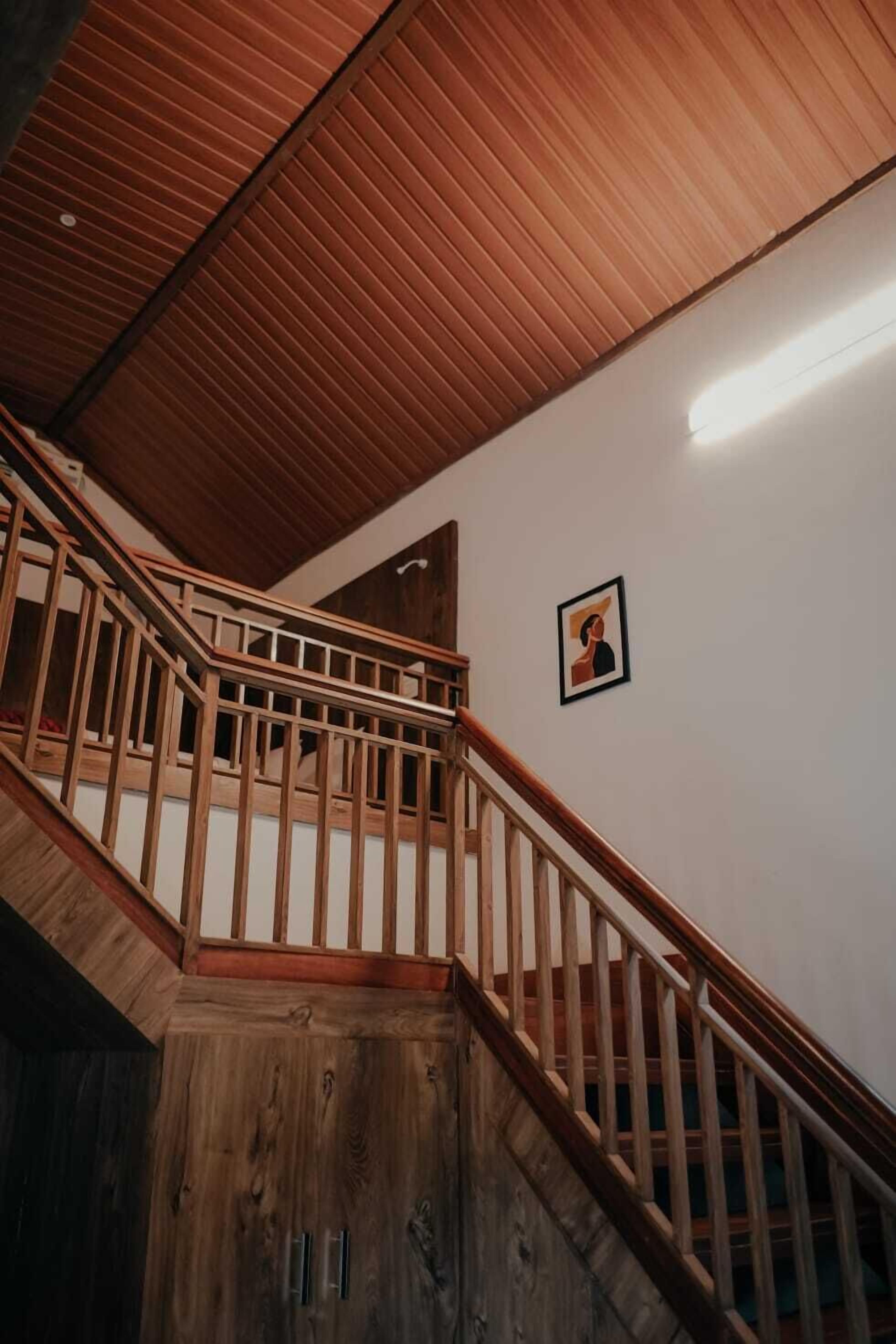 A wooden staircase with a railing, a framed picture on the wall, and a ceiling with wooden panels.