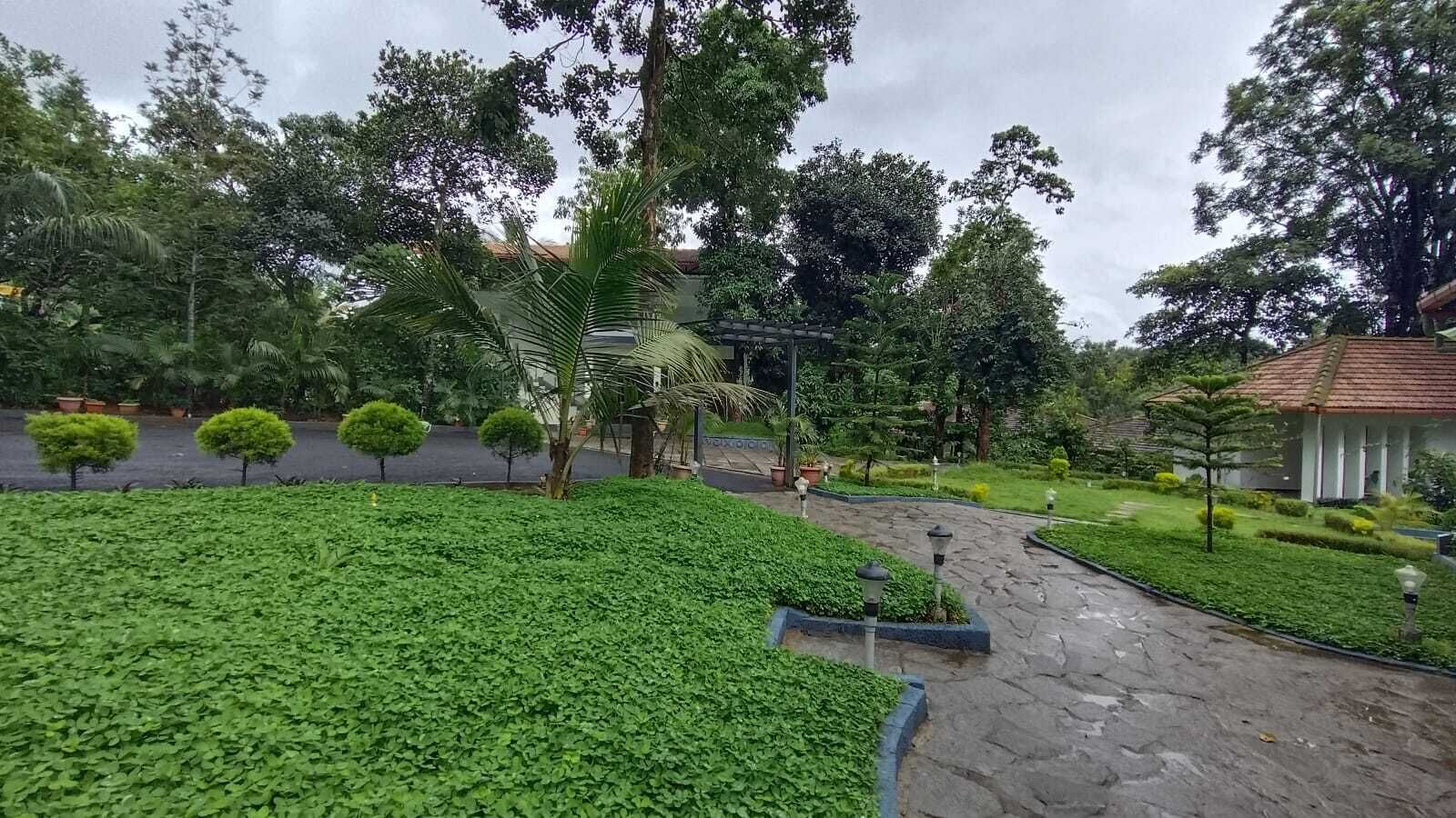 A landscaped garden with a paved walkway, neatly trimmed hedges, and a variety of trees.