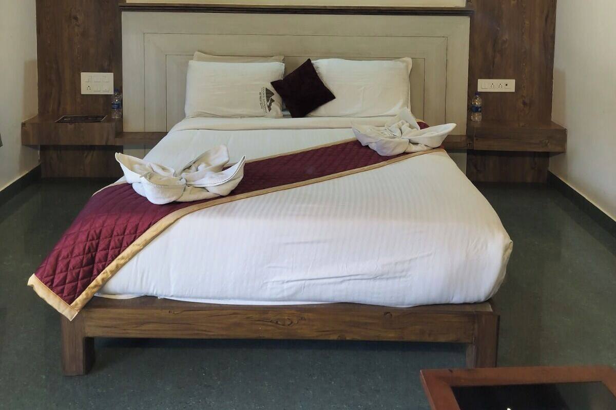 A neatly made bed with white linens and a red throw blanket, wooden headboard, and two nightstands with water bottles.