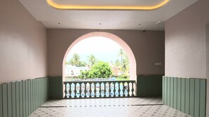 Ein Zimmer mit einem gemusterten Boden, einem Balkon mit Geländer und Blick auf Grünflächen und Gebäude.