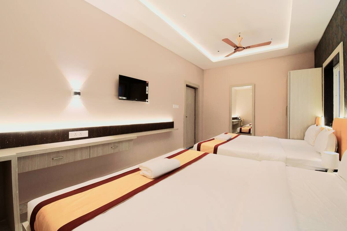 A hotel room with two beds, a flat-screen TV, a ceiling fan, and a large mirror.