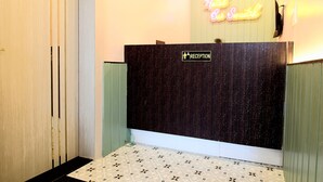 Ein Hotel-Empfangsbereich mit einem Neonzeichen, das 'Hotel Cat Swastik' zeigt, einem Empfangsschalter und einem gemusterten Boden.