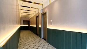 Ein Korridor mit gemustertem Bodenbelag, grünen Wandverkleidungen und Türen zu Zimmern.