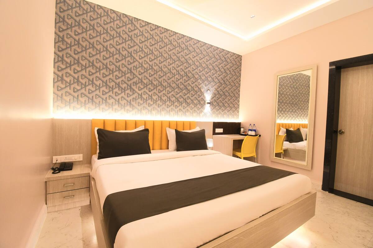 A modern hotel room with a large bed, bedside tables, a mirror, and a patterned wall.