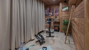 Une pièce aux murs en bois, avec un ventilateur de plafond, un tapis de course, une bouteille d’eau et une petite table.