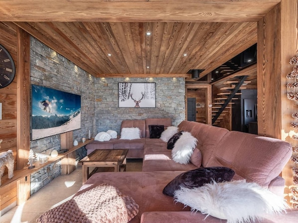 A cozy living room with a stone wall, wooden ceiling, and a large flat-screen TV.