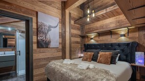 Une chambre avec un plafond en bois, un grand lit doté d’une literie moelleuse, une tête de lit et une table de chevet avec une lampe.