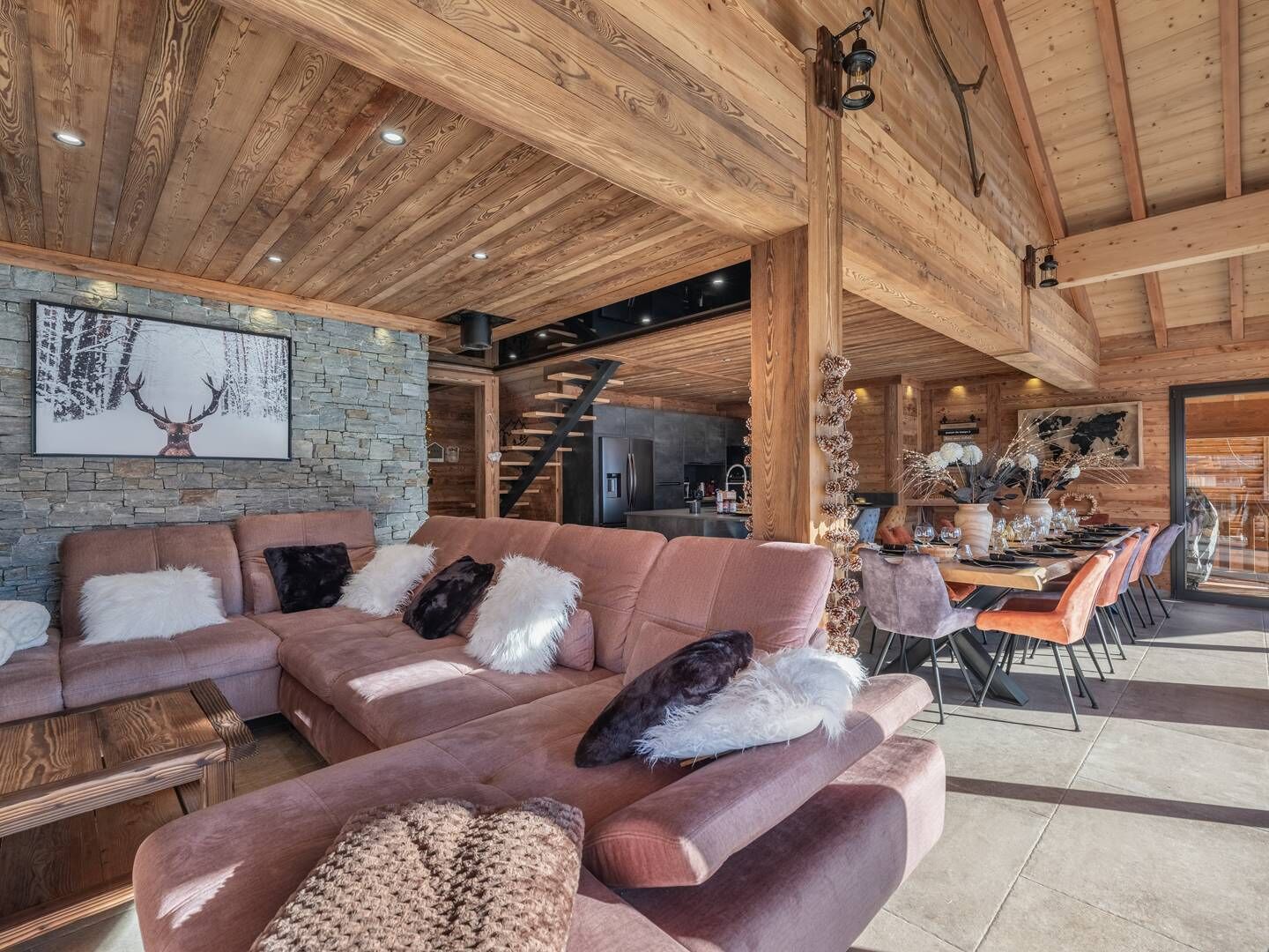 A spacious living area with a large sectional sofa, a stone accent wall, and a wooden ceiling.