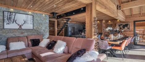 A spacious living area with a large sectional sofa, a stone accent wall, and a wooden ceiling.