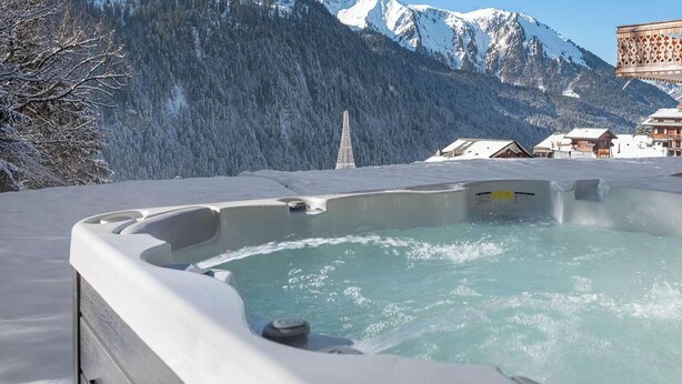 Een hottub met uitzicht op besneeuwde bergen en een houten gebouw.