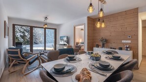 Een moderne eetruimte met een houten tafel voor vier personen, een gezellige zithoek en een uitzicht op met sneeuw bedekte bomen door grote ramen.
