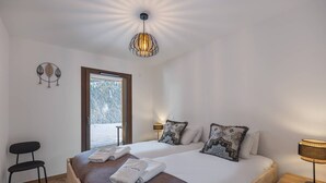 Een slaapkamer met een groot bed, een houten nachtkastje, een stoel en een plafondlamp.