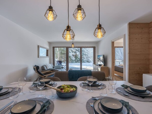 A dining area with a table set for six, a bowl of salad, and a television in the background.