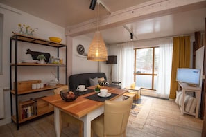 Ett mysigt vardagsrum med ett matbord i trä, en soffa, en tv och en bokhylla.