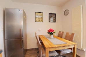 Una cocina funcional con un refrigerador de acero inoxidable, una mesa de madera con cuatro sillas y dos cuadros en la pared.