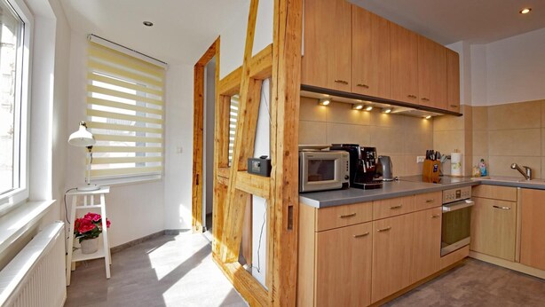 A modern kitchen with wooden cabinets, a microwave, a kettle, and a small table with a lamp.
