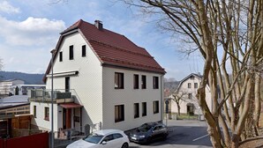 A two-story building with a red roof, a balcony on the upper floor, and a parked white car in front.