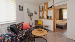 A living room with a sofa, a small round table, a chair, and a bed in the background.