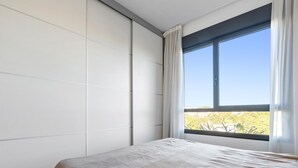 A bedroom with a bed, a large window with curtains, and a view of trees outside. - Apartment with pool and paddle tennis 500m beach (Torredembarra)