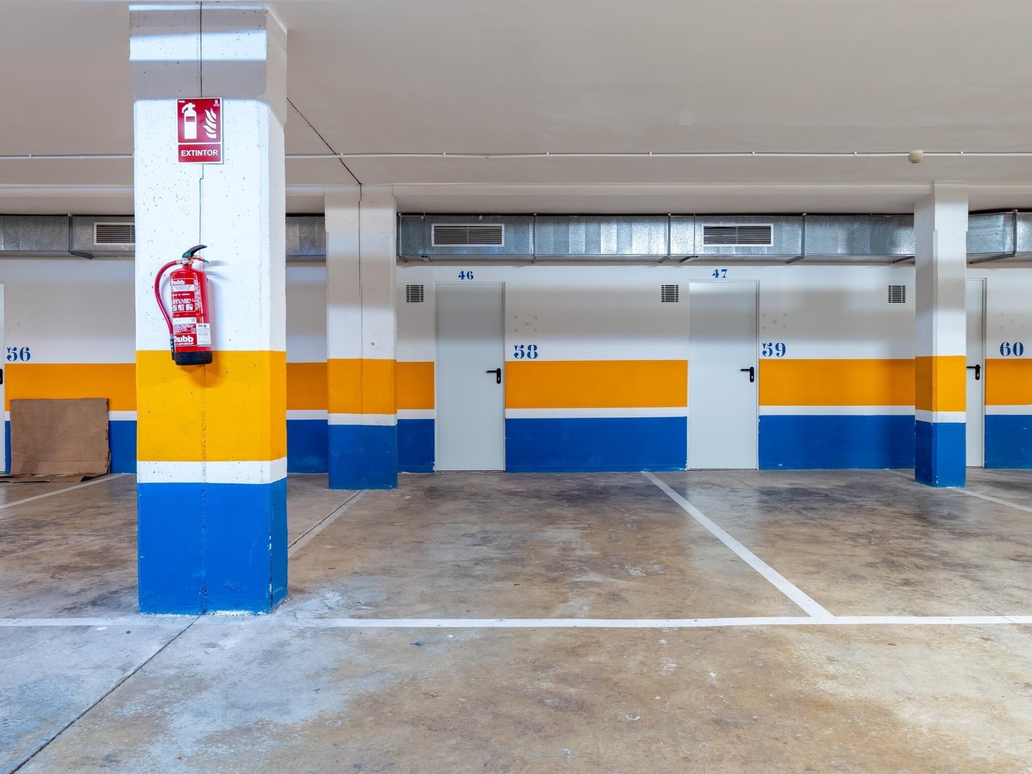 A parking garage with numbered parking spaces, fire extinguishers, and ventilation grilles on the ceiling.