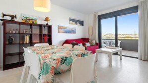 A modern living room with a dining table, a red sofa, and a bookshelf. - Apartment with pool and paddle tennis 500m beach (Torredembarra)
