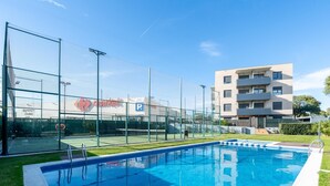 A swimming pool with a netted area, a parking sign, and a multi-story building in the background. - Apartment with pool and paddle tennis 500m beach (Torredembarra)