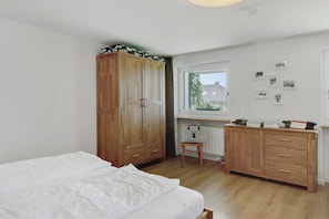A bedroom with a bed, wooden wardrobe, a small stool, a radiator, and a window with pictures on the wall. - Apartment 'Staffe' with Mountain View, Private Terrace and Wi-Fi (Bonndorf im Schwarzwald)