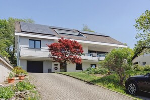 A modern two-story house with solar panels, a paved driveway, and a red tree. - Apartment 'Staffe' with Mountain View, Private Terrace and Wi-Fi (Bonndorf im Schwarzwald)