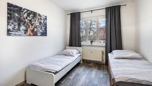 A bedroom with two single beds, a window with curtains, a radiator, and a deer painting on the wall. - Apartment 'Auf Zeit' with Wi-Fi (Leipzig)