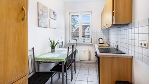 A compact kitchen with wooden cabinets, a dining table, and a window with a view of houses. - Apartment 'Auf Zeit' with Wi-Fi (Leipzig)