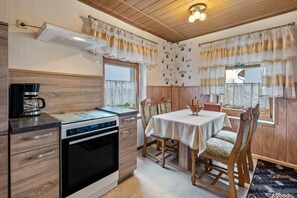 Eine Küche mit Herd, Backofen und Kaffeemaschine, Holzausstattung und einem Essbereich mit Tisch und Stühlen.