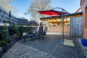 Une terrasse extérieure avec une table et des chaises, un parasol rouge et un mur en briques.