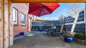 A patio area with a red umbrella, outdoor seating, potted plants, and a brick wall. - Apartment 'Fewo 1' with Private Terrace and Wi-Fi (Klink)
