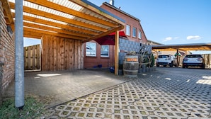 A covered outdoor area with a wooden pergola, a brick building, and two cars parked under a canopy. - Apartment 'Fewo 1' with Private Terrace and Wi-Fi (Klink)