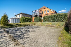 Un quartier résidentiel avec une allée pavée, une maison dotée d’un balcon et une haie.