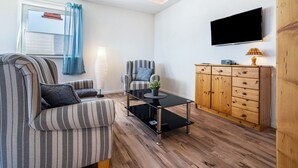 A living room with striped sofas, a glass coffee table, a wooden cabinet, and a mounted TV. - Apartment 'Fewo 1' with Private Terrace and Wi-Fi (Klink)