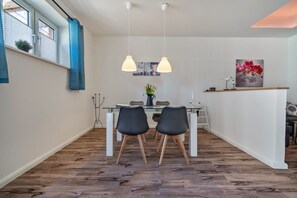 Un espace de salle à manger moderne avec une table en verre, des chaises noires, des luminaires suspendus et une vue sur l’extérieur.