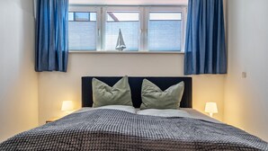 Ein ordentlich bezogenes Bett mit einer gemusterten Decke, zwei Kissen und einem Fenster mit Vorhängen.