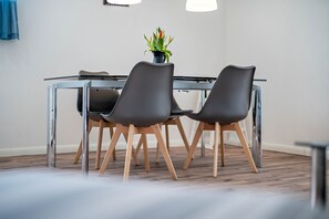 Un comedor moderno con una mesa de vidrio, sillas oscuras y piso de madera.